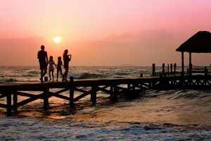 Photo by Pixabay Silhouetted family enjoys a stroll on the beach pier at a vibrant sunset over the ocean waves.